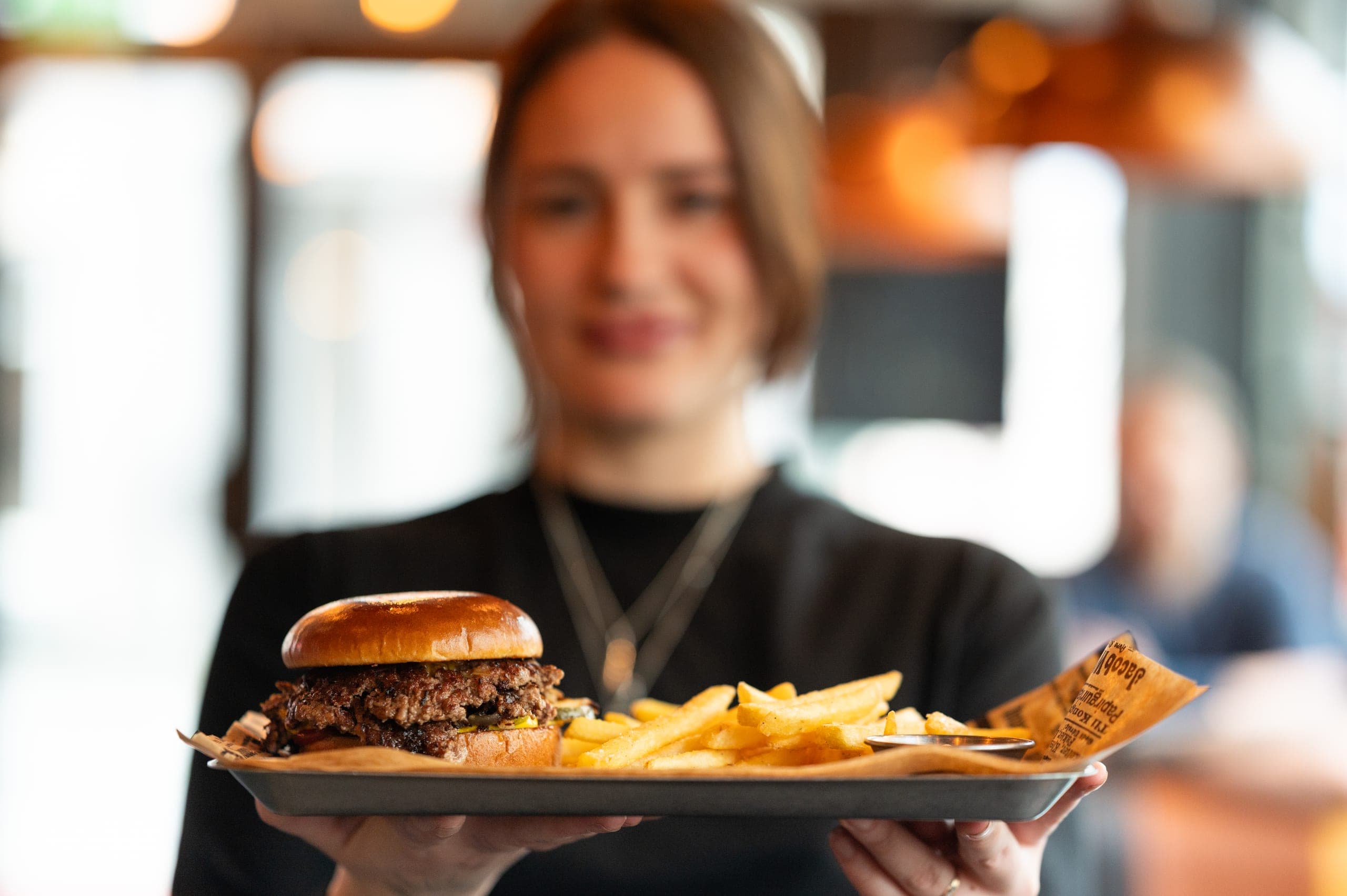 Servitør med smashburger og fries på brett